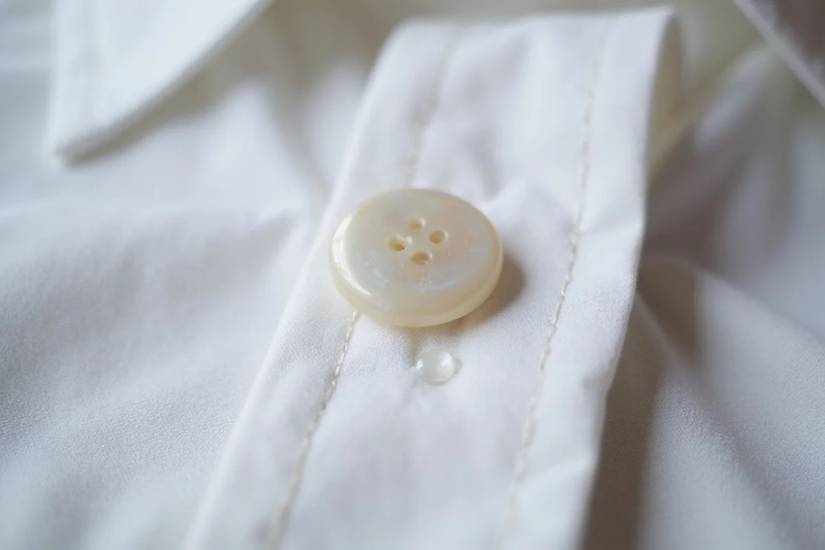 Close detail of a mother-of-pearl button on a crisp white cotton shirt